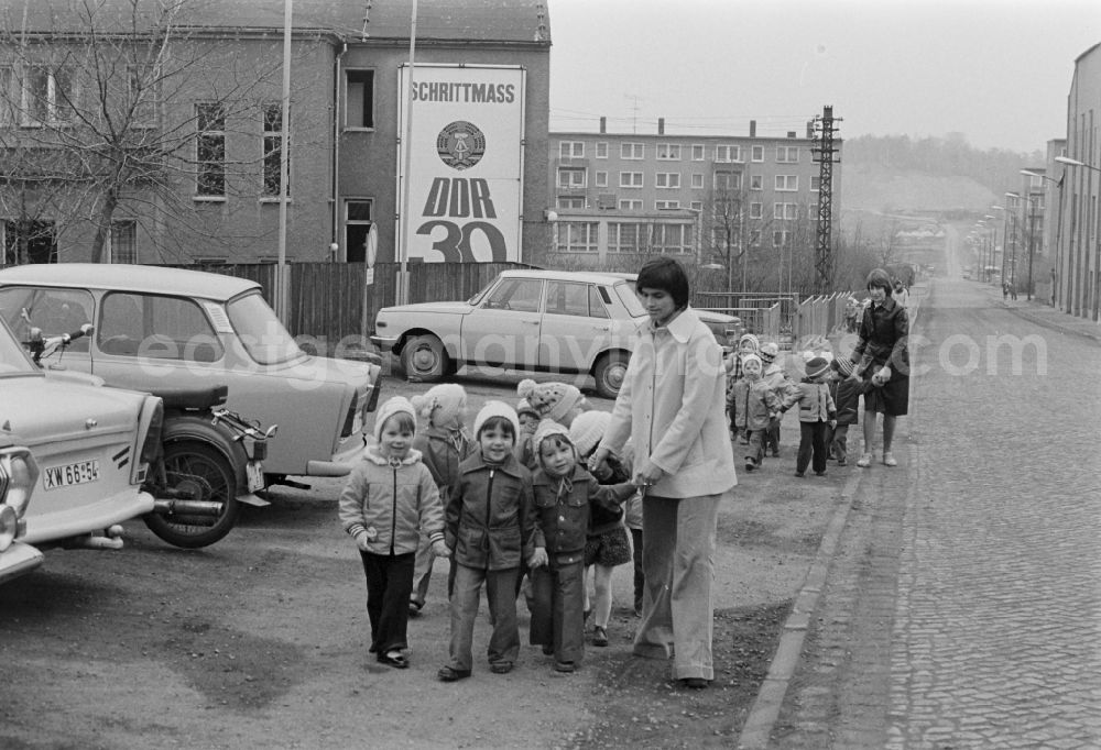 GDR image archive: Brand-Erbisdorf - Educators look after small children in groups on the sidewalk of a street in front of the background of a propaganda poster Schrittmass DDR 3