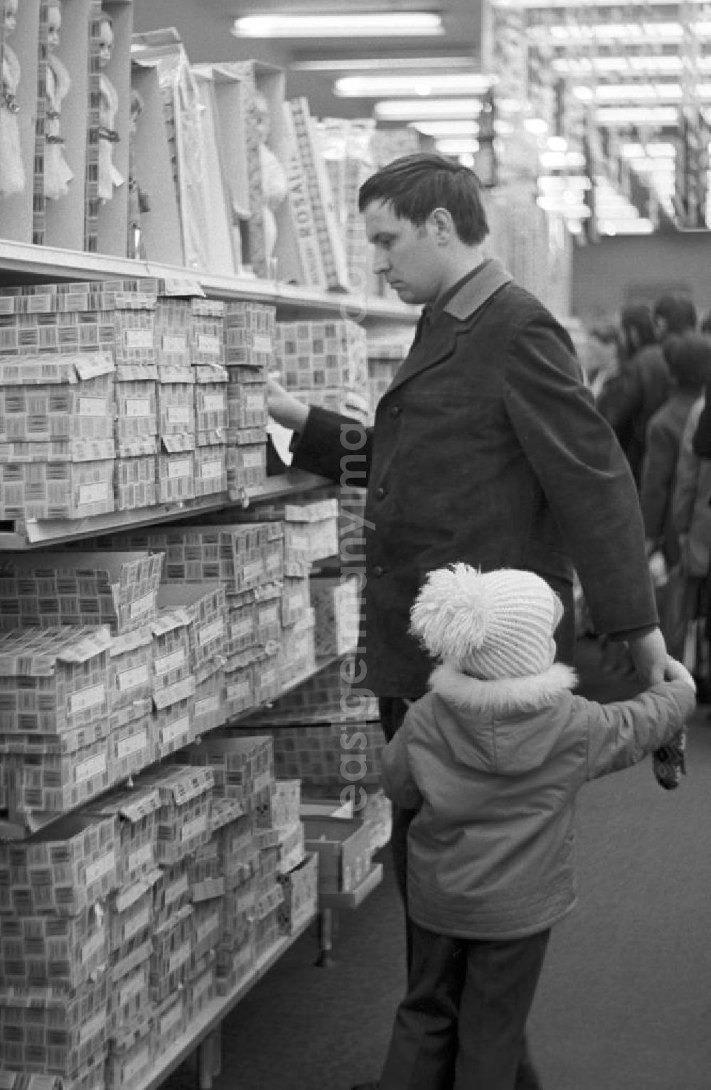 GDR picture archive: Berlin - Ein Mann steht mit seinem Kind vor einem Regal mit Anziehpuppen in der Spielzeugabteilung im Centrum Warenhaus in Berlin.