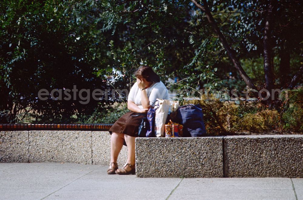 GDR image archive: Berlin - Woman taking a break with full shopping bags on a park bench in East Berlin on the territory of the former GDR, German Democratic Republic