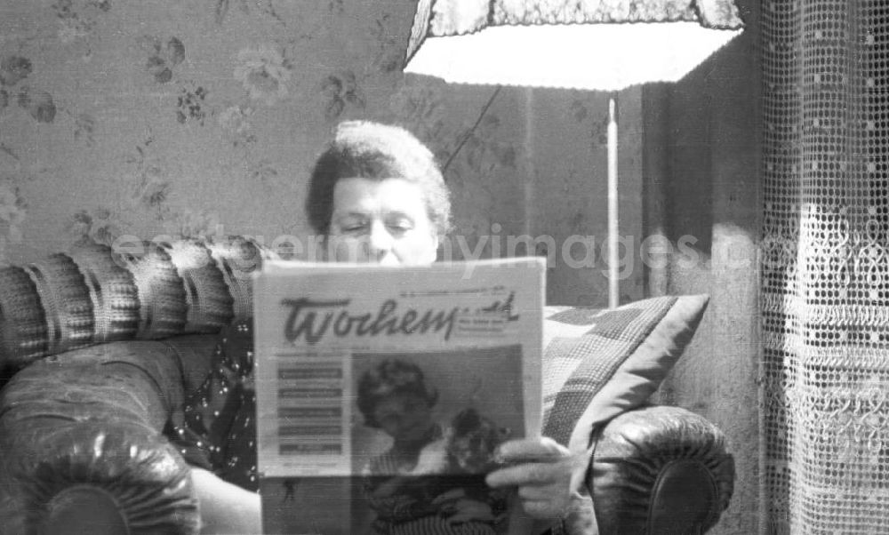 GDR picture archive: Leipzig - Eine Frau liest im Wohnzimmer auf einem Sessel eine Ausgabe der Wochenpost. Das Titelbild zeigt ein junges Mädchen mit einem Löwenjungen im Arm. Bestmögliche Qualität nach Vorlage!