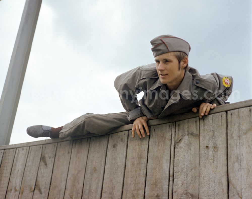 GDR picture archive: Berlin - Young man overcomes an escalator wall during pre-military training on the Sturmbahn as part of the Society for Sports and Technology in Berlin, East Berlin in the territory of the former GDR, German Democratic Republic