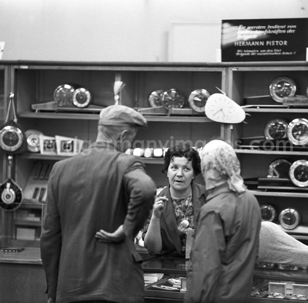 GDR picture archive: Leipzig - Verkaufsgespräch in der Uhrenabteilung in einem Kaufhaus in Leipzig. Auf dem Regal steht ein Schild mit der Aufschrift Sie werden bedient von Fachverkaufskräften der Brigade Hermann Pistor.