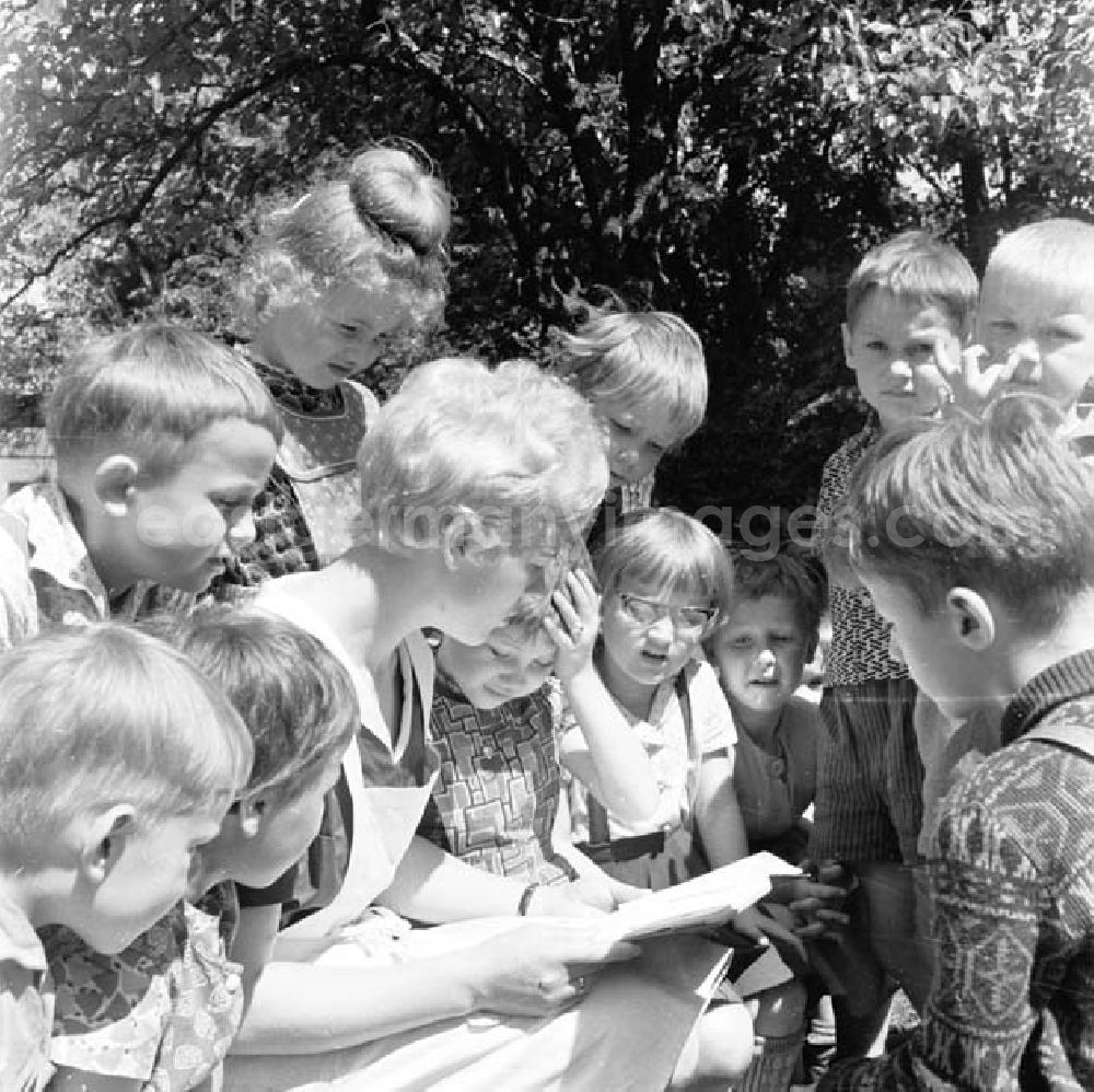 Brandenburg: Erzieherin und Kinder / Kleinkinder aus Kindergarten / Kita sitzen zusammen. Erzieherin liest aus einem Buch vor.