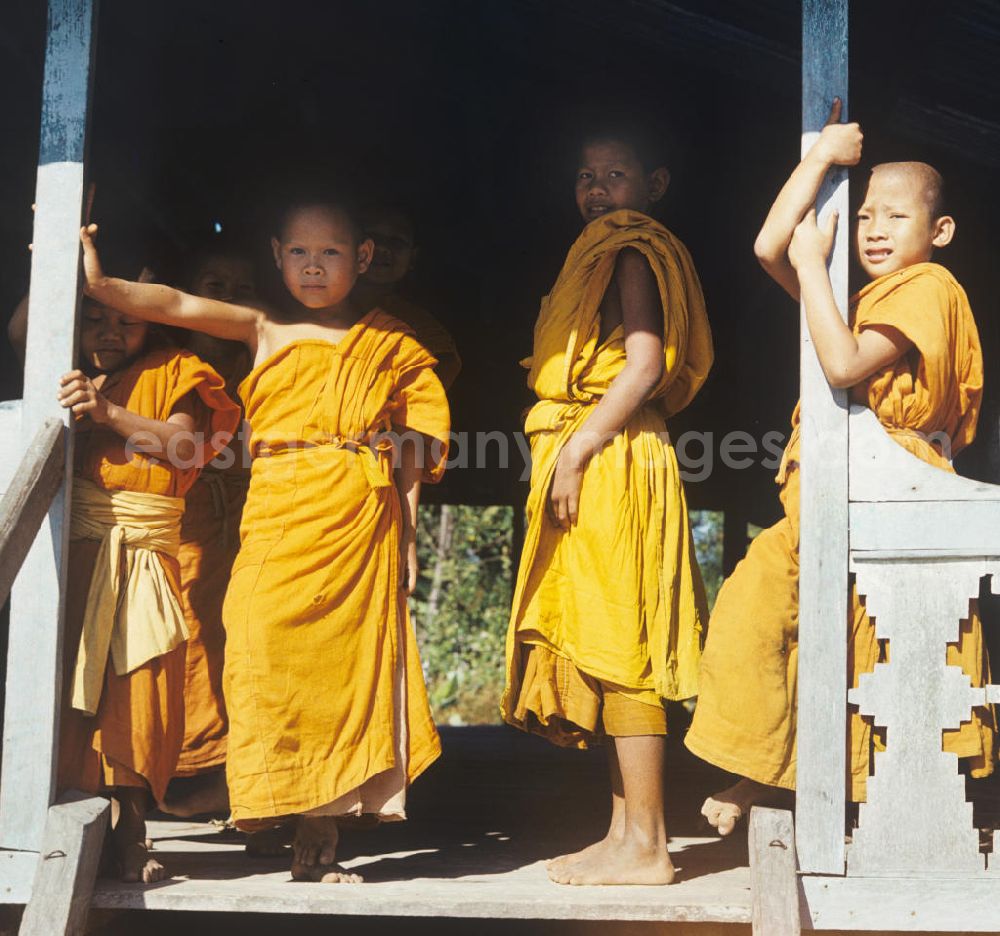 Vientiane: Kindermönche / Mönche in den charakteristischen safrangelben Gewändern in einem buddhistischen Tempel in Vientiane, der Hauptstadt der Demokratischen Volksrepublik Laos. Bis zur Ausrufung der Volksrepublik Laos am 2. Dezember 1975 bestimmte der Theravada-Buddhismus die kulturelle Entwicklung im Land. Nachdem die anfängliche Unterdrückung der traditionellen buddhistischen Bräuche durch die neuen kommunistischen Machthaber mißlang, fand Laos in den folgenden Jahrzehnten einen eigenen Weg der Koexistenz von Buddhismus und Sozialismus.