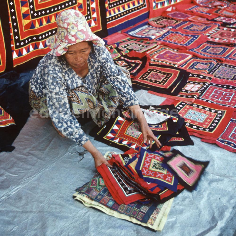 GDR picture archive: Vientiane - Eine Frau aus dem Volksstamm der Meo, auch Hmong genannt, verkauft selbstgenähte Decken in Vientiane, der Hauptstadt der Demokratischen Volksrepublik Laos. Die Hmong gehörten zu einer infolge des Vietnam-Krieges verfolgten und zurückgezogen lebenden Minderheit in Laos.