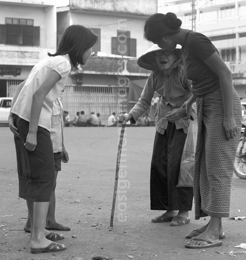 GDR picture archive: Vientiane - Zwei junge Frauen kümmern sich um eine Greisin auf einer Straße in Vientiane, der Hauptstadt der Demokratischen Volksrepublik Laos.