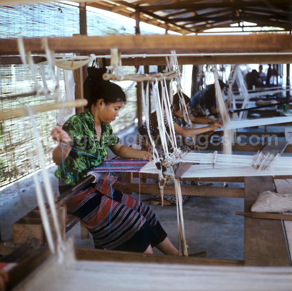 GDR photo archive: Vientiane - Frauen weben an Holzwebstühlen in einer Weberei in Vientiane, der Hauptstadt der Demokratischen Volksrepublik Laos.