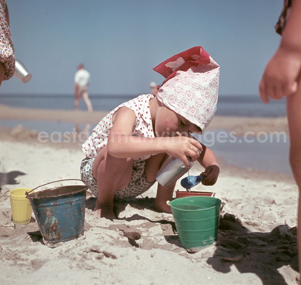 Binz: Little girl with headscarf digs on the sandy beach of the Baltic Sea during her Baltic Sea vacation in Binz, Mecklenburg-Western Pomerania in the territory of the former GDR, German Democratic Republic