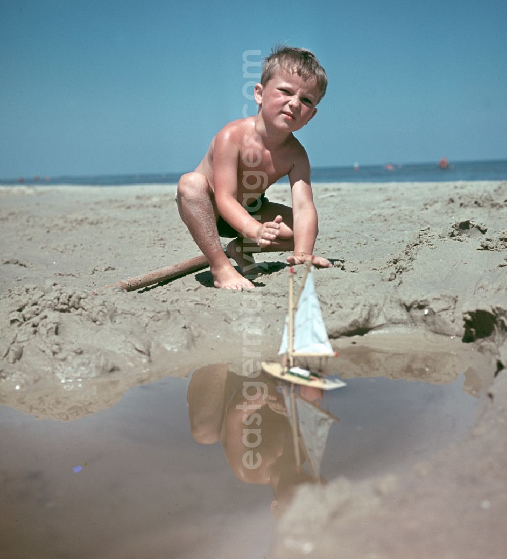 GDR picture archive: Binz - Little boy plays with a boat on the sandy beach of the Baltic Sea during a Baltic Sea vacation in Binz, Mecklenburg-Western Pomerania in the territory of the former GDR, German Democratic Republic