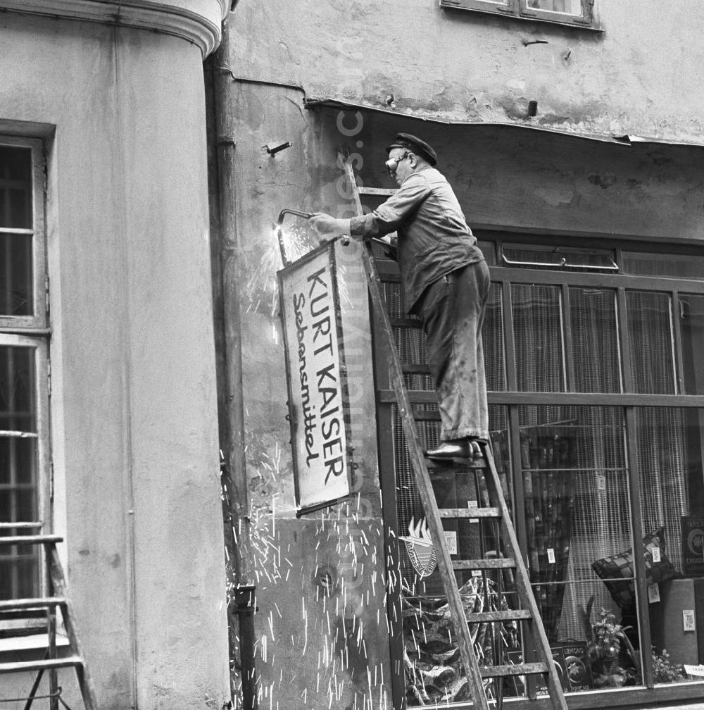 GDR photo archive: Rostock - Ein Mann montiert das Schild des Lebensmittelladens Kurt Kaiser in Rostock ab. Das Geschäft mußte einem Textilladen weichen.