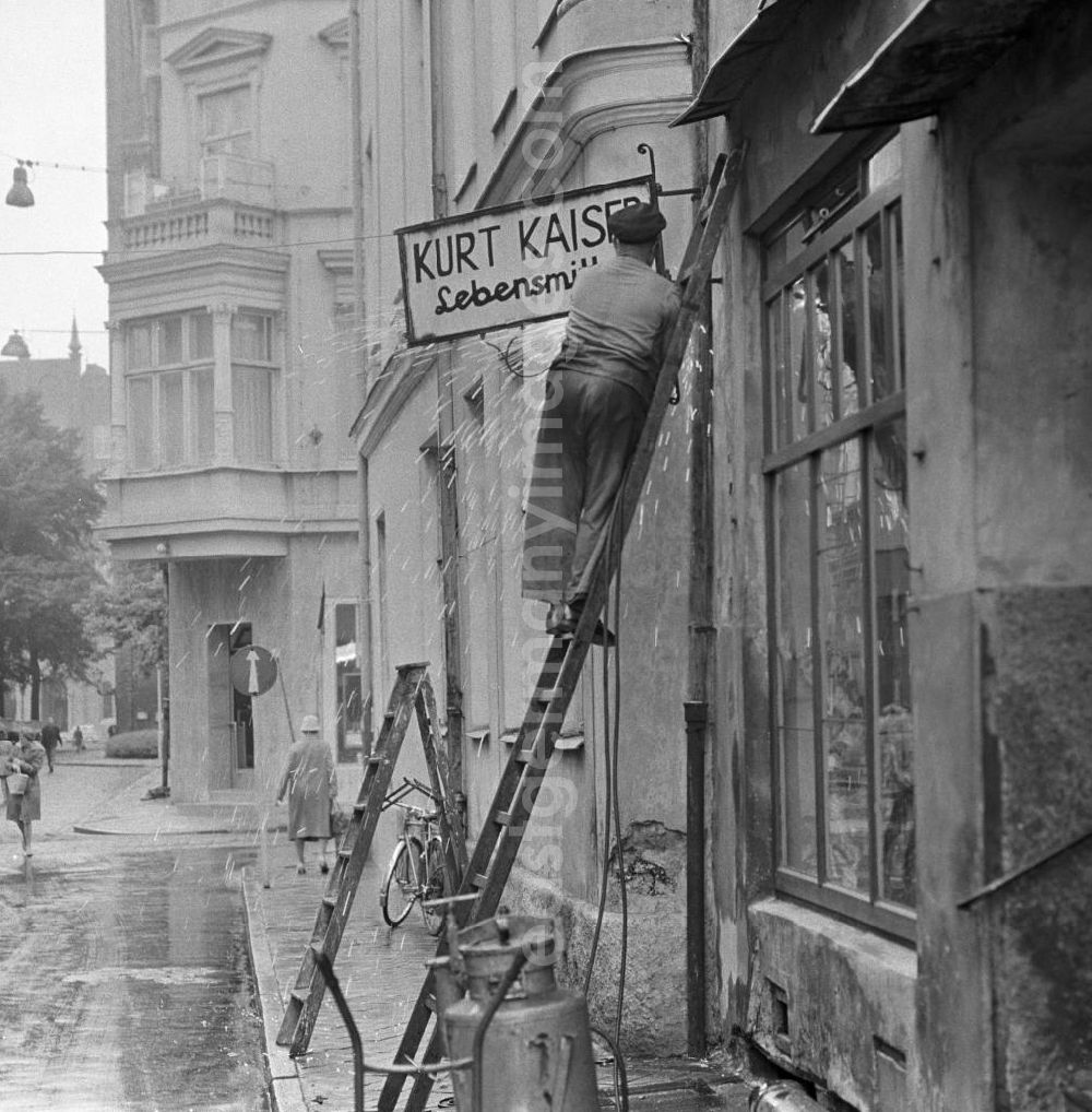 GDR picture archive: Rostock - Ein Mann montiert das Schild des Lebensmittelladens Kurt Kaiser in Rostock ab. Das Geschäft mußte einem Textilladen weichen.