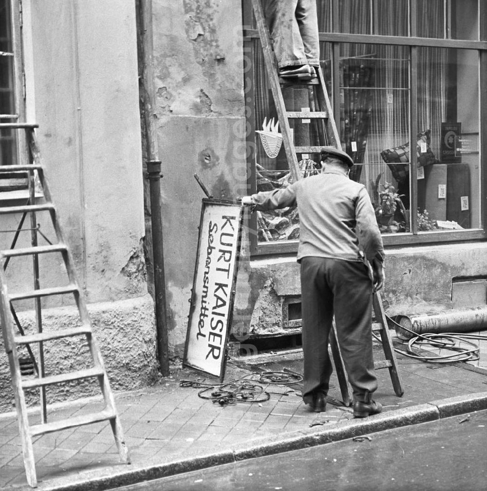 Rostock: Zwei Männer montieren das Schild des Lebensmittelladens Kurt Kaiser in Rostock ab. Das Geschäft mußte einem Textilladen weichen.