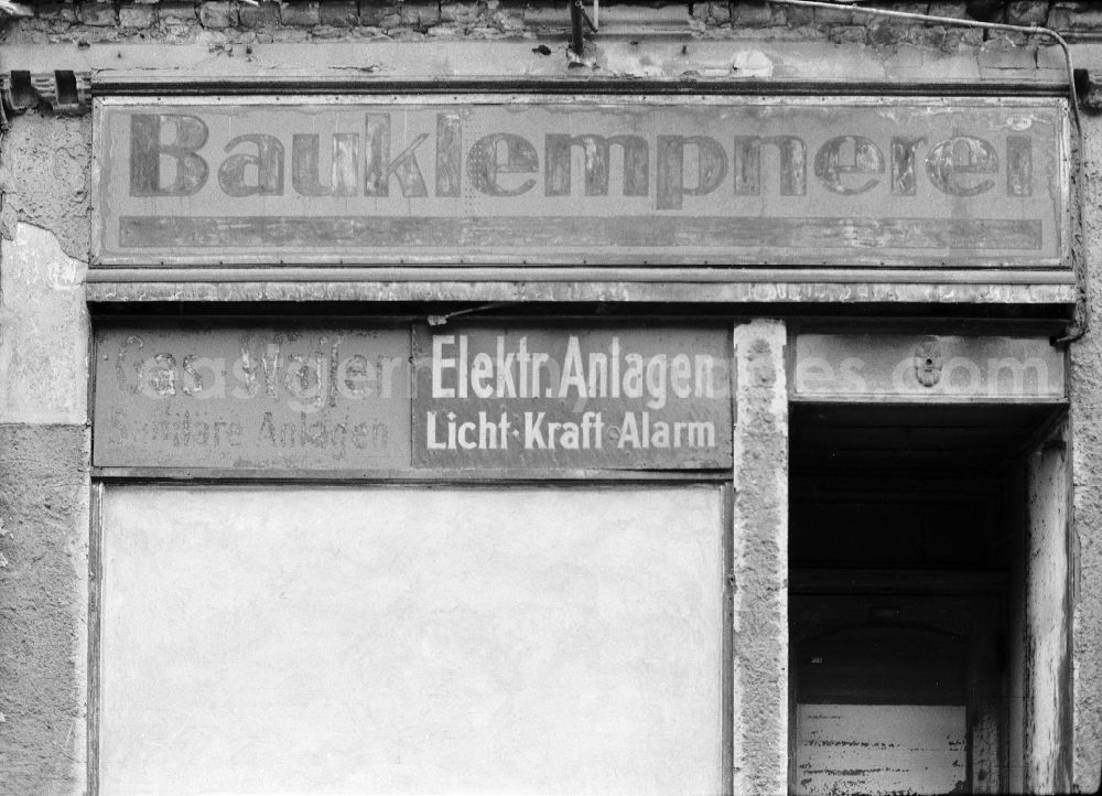 Berlin: Fading lettering in the entrance area and shop window of a retail store Bauklempnerei - Gas - Wasser - Elektrische Anlagen in the street area of an old residential building facade on Schwedter Strasse in the district of Prenzlauer Berg in Berlin East Berlin in the area of the former GDR, German Democratic Republic