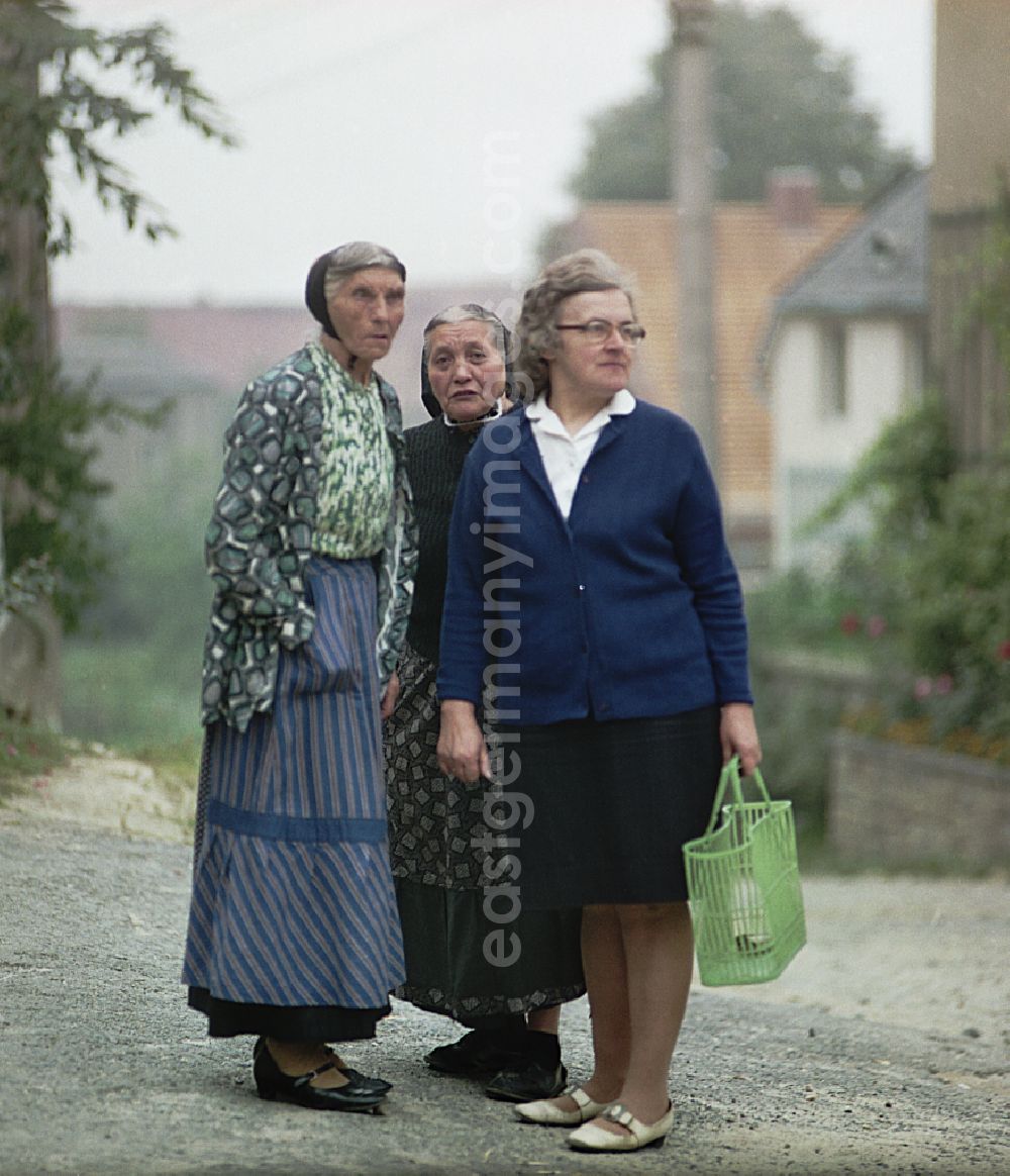 GDR image archive: Räckelwitz - Three women stand on a village street. Two older women wear Sorbian everyday costume as a scene from the film and television production Portrait of a Center on the main street in Raeckelwitz, Saxony in the area of the former GDR, German Democratic Republic