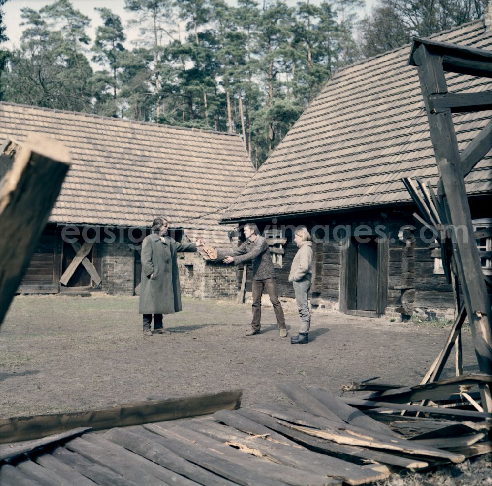 GDR photo archive: Weißkeißel - Scene from the film and television production Rublak - The Legend of the Surveyed Land in the Haide district of Weisskeissel, Saxony in the area of the former GDR, German Democratic Republic. The actor Christian Grashof hands the actor Hans-Uwe Bauer a violin. The actress Johanna Schall observes the events in the courtyard of a farmhouse