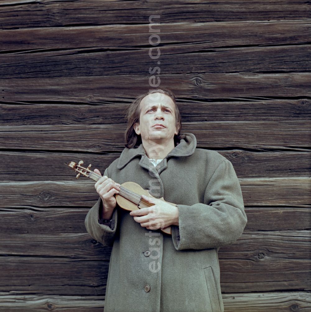 GDR image archive: Boxberg - Scene from the film and television production Rublak - The Legend of the Surveyed Land Waste Landscape in Lusatia - the actor Christian Grashof stands with a violin in his arm at the wooden wall of the village church in the Spey district of Boxberg in the GDR