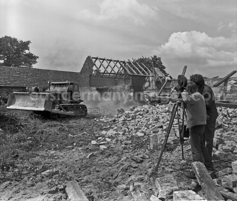 GDR picture archive: Braunkohlentagebau - Scene from the film and television production Struga - Pictures of a Landscape in a demolition area for a brown coal open-cast mine in the Lausitz region of Saxony in the area of the former GDR, German Democratic Republic. A tracked excavator is tearing down an old abandoned farmstead