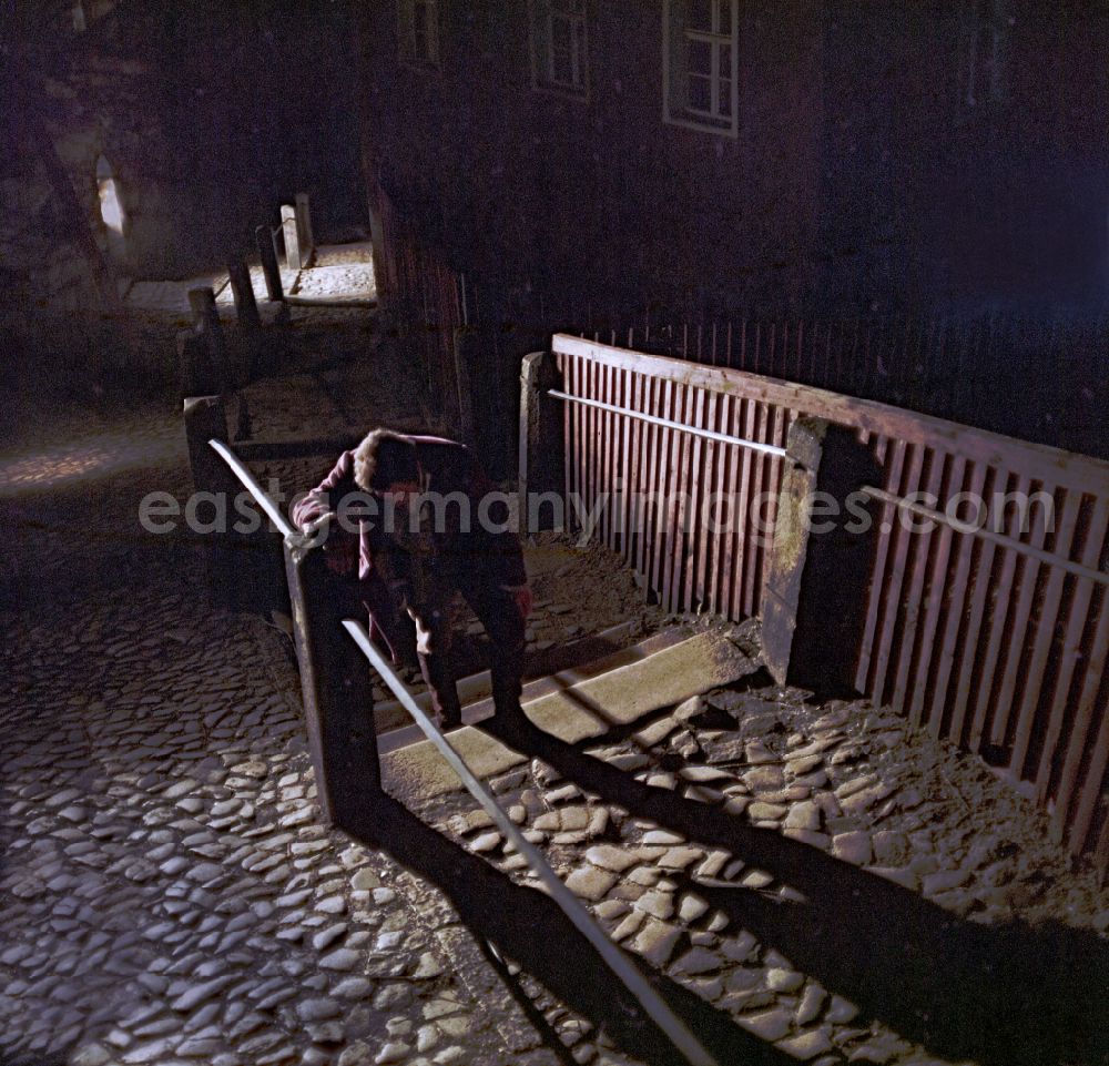 GDR image archive: Bautzen - Scene photo for the film: Continent Hope An evening street with cobblestones. A man with a straw broom (Mericin Slowdenk) carries a bald man (Axel Reinsahen) piggyback, who is drinking from a clay jug. A woman in a headscarf (Majka Ulbrichec) runs after them in the background