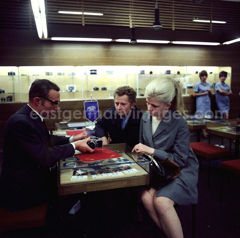 GDR picture archive: Berlin - Verkaufsgespräch im Fotofachgeschäft des Kombinates Zeiss am Alexanderplatz in Berlin Mitte. Kunden interessieren sich für eine Kleinbildkamera der Marke Praktika.