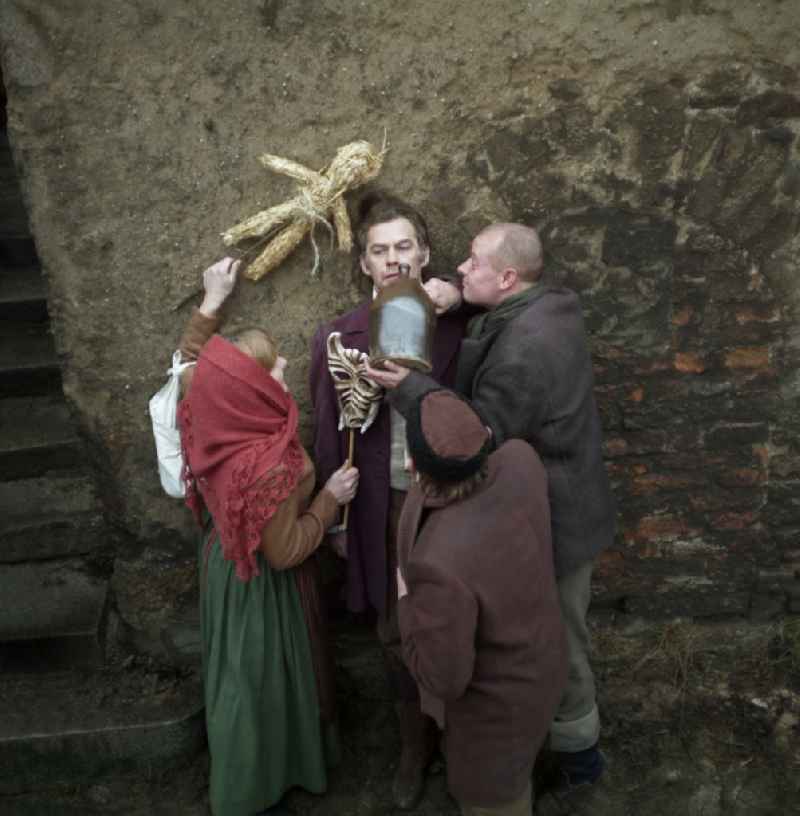 Scene photo for the film: 'Continent Hope' The actor Manfred Schulz as the painter Heinrich Theodor Wehle is harassed by a woman in a headscarf (Majka Ulbrichec) and a man with a straw broom (Mericin Slowdenk). A bald man (Axel Reinshagen) forces him to drink with a clay jug