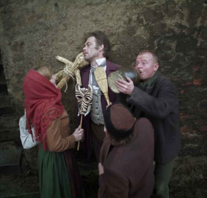 Scene photo for the film: 'Continent Hope' The actor Manfred Schulz as the painter Heinrich Theodor Wehle is harassed by a woman in a headscarf (Majka Ulbrichec) and a man with a straw broom (Mericin Slowdenk). A bald man (Axel Reinshagen) drinks from a clay jug