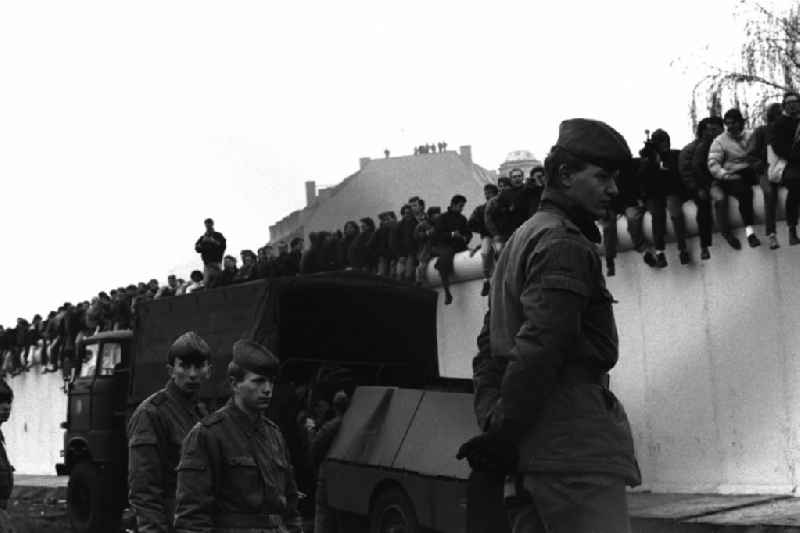 Besetzung der Grenzanlagen am Potsdamer Platz. Soldaten der DDR stehen vor der Berliner-Mauer, auf der Mauer sitzen und stehen Menschen.