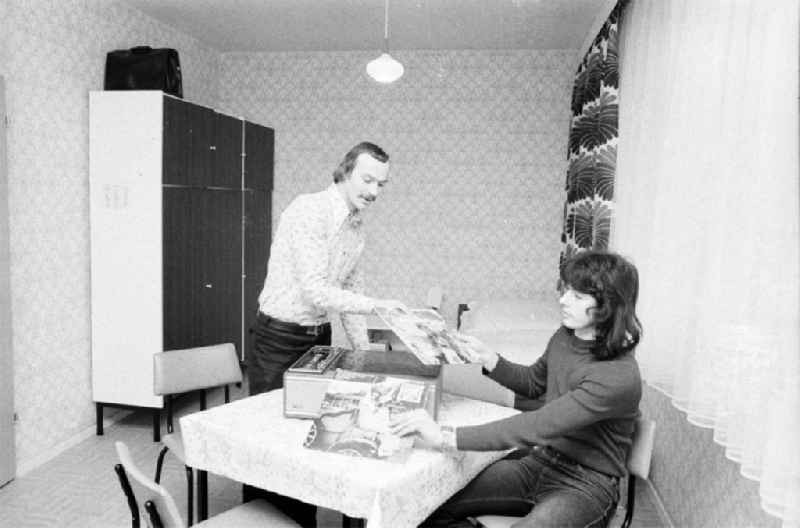 Blick in Zimmer des Arbeiterwohnheim an der Rhinstraße / Ecke Landsberger Allee, dem heutigen COMFORT Hotel. Zwei Männer mit Schallplatten vor einem Schallplattenspielen auf Tisch. Tapete und Vorhänge im 7