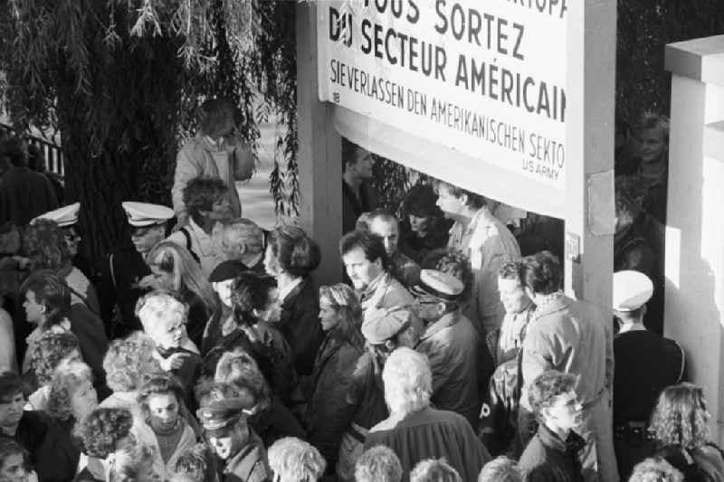 Menschen passieren den Grenzübergang Oberbaumbrücke. Sie gehen unter ein Schild mit der Aufschrift '...SIE VERLASSEN DEN AMERIKANISCHEN SEKTOR' hindurch.