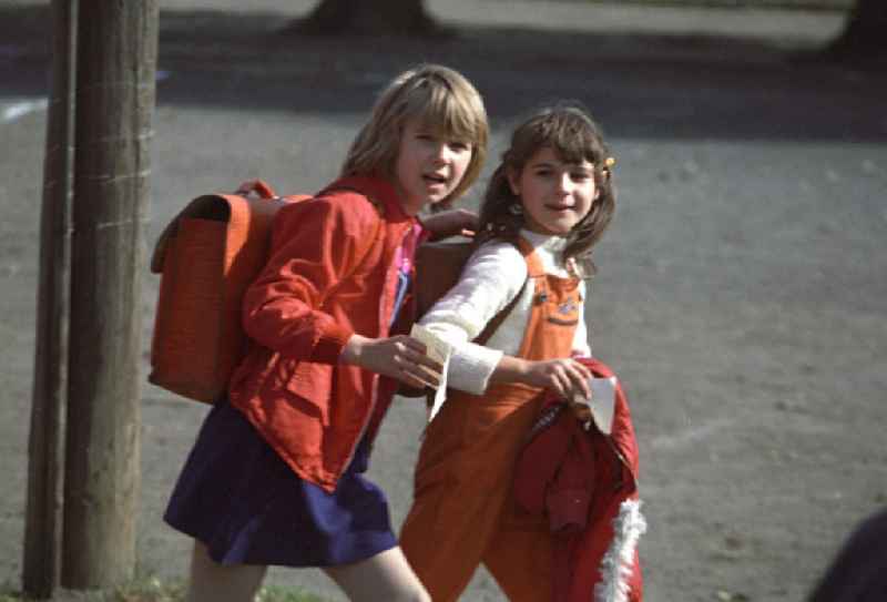 Zwei Mädchen mit Lederranzen gehen nach dem Ende der letzten Unterrichtsstunde über den Sportplatz einer Berliner Schule nach Hause. Obwohl es in der DDR eine gut ausgebaute Hortbetreuung gab, durften viele Schüler bereits in den ersten Klassen sogenannte Schlüsselkinder sein. Sie hatten von ihren Eltern die Erlaubnis, nach der Schule allein nach Hause zu gehen und verbrachten ihre Freizeit oft mit Freunden. Die Eltern waren meist beide berufstätig und kamen erst zum Abendbrot nach Hause.