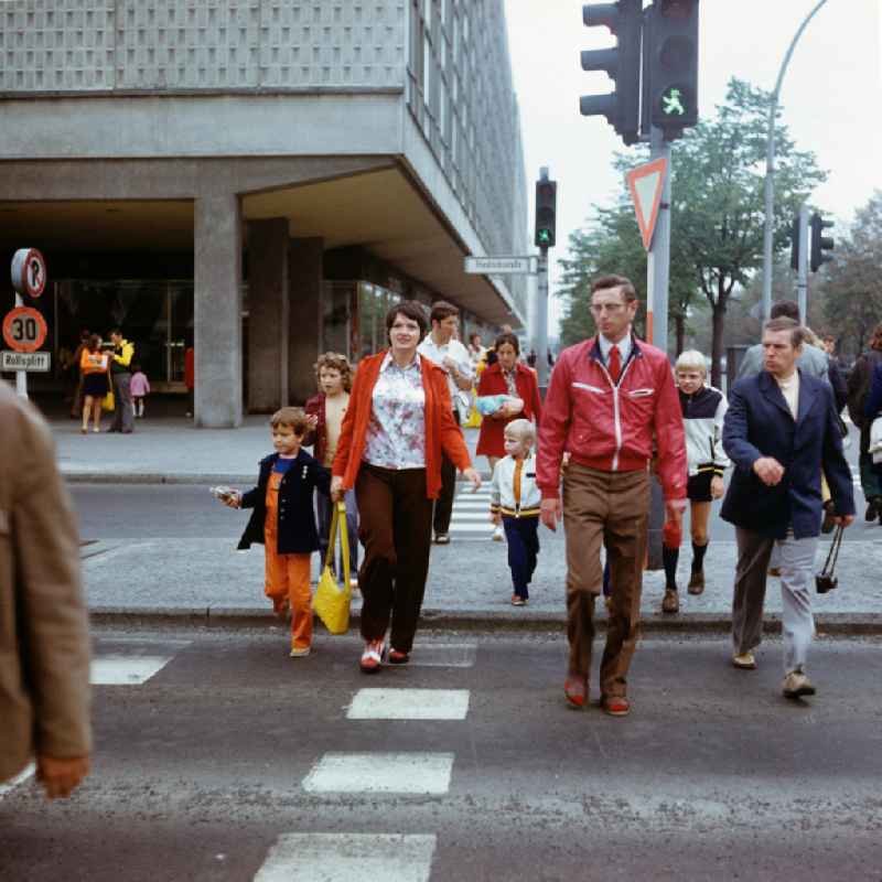 Passanten gehen an einer grünen Ampel an der Kreuzung Friedrichstraße / Ecke Unter den Linden in Berlin-Mitte über die Straße, im Hintergrund die Ladenpassage des Grand-Hotel.