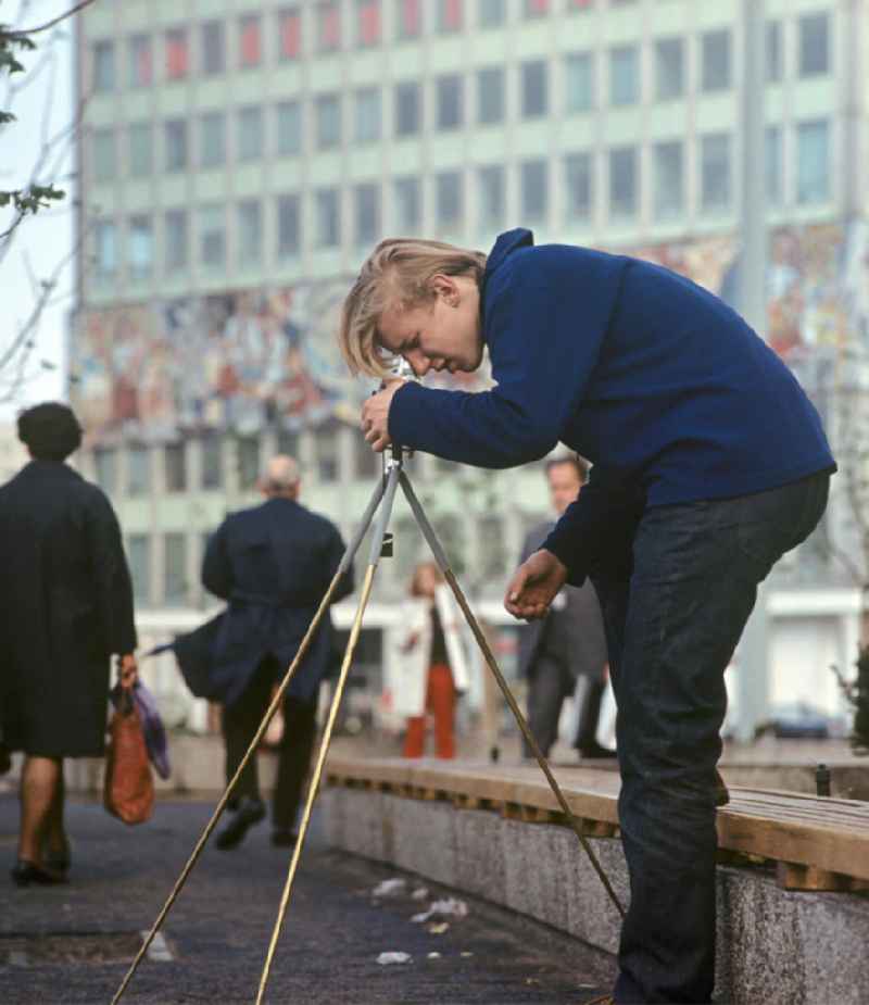 Ein Fotograf fotografiert mit Stativ den Alexanderplatz. Für viele Fotografen bietet der neu gestaltete Alexanderplatz in Berlins neuer Mitte ein besonders interessantes Motiv. Gebäude wie das Haus des Lehrers im Hintergrund sowie eine großflächige Umgestaltung des Alex sollten Ost-Berlin als Hauptstadt der DDR das Antlitz einer sozialistischen Großstadt verleihen.