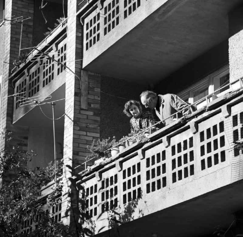 Ein älteres Ehepaar steht auf dem Balkon seiner Wohnung in Berlin Mitte - während er die Balkonblumen inspiziert, blickt sie interessiert zum Fotografen. Neben den Blumenkästen verzieren Antennen die Fassade der Balkone.