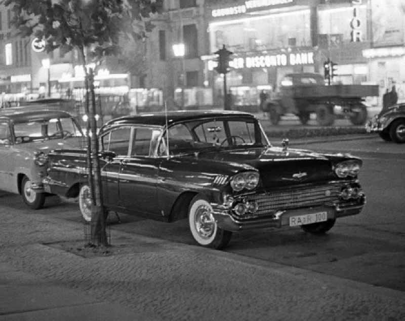 Ein Chevrolet Bel Air - ein amerikanischer PKW der oberen Mittelklasse - parkt auf dem Kurfürstendamm in Westberlin. Im Hintergrund Leuchtreklame wohin das Auge blickt - als Schaufenster des Westens und Symbol des Wirtschaftswunders erstrahlt der Ku'damm, Westberlins wichtigste Flaniermeile, auch abends in hellem Licht. In den 5