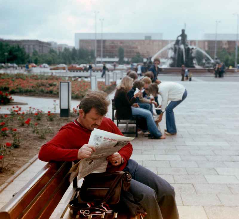 Ein Mann sitzt an den Wasserspielen am Berliner Fernsehturm in Berlin und liest die BZ am Abend. Im Hintergrund der Neptunbrunnen und der Palast der Republik.