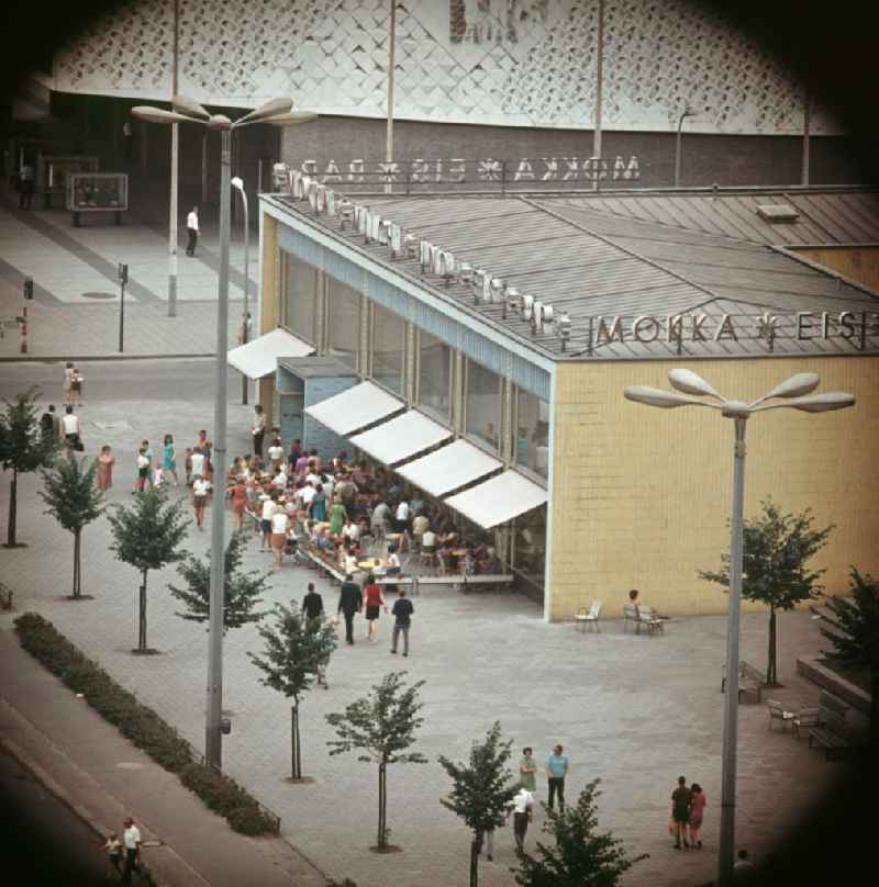 Moderne Neubauten sollen Ost-Berlin als Hauptstadt der DDR das Antlitz einer sozialistischen Großstadt verleihen - hier Blick auf die beliebte Mokka-Milch-Eisbar an der Karl-Marx-Allee, dahinter das Kino International. Der bestehende Wohnungsmangel entwickelte sich in der DDR seit den 6