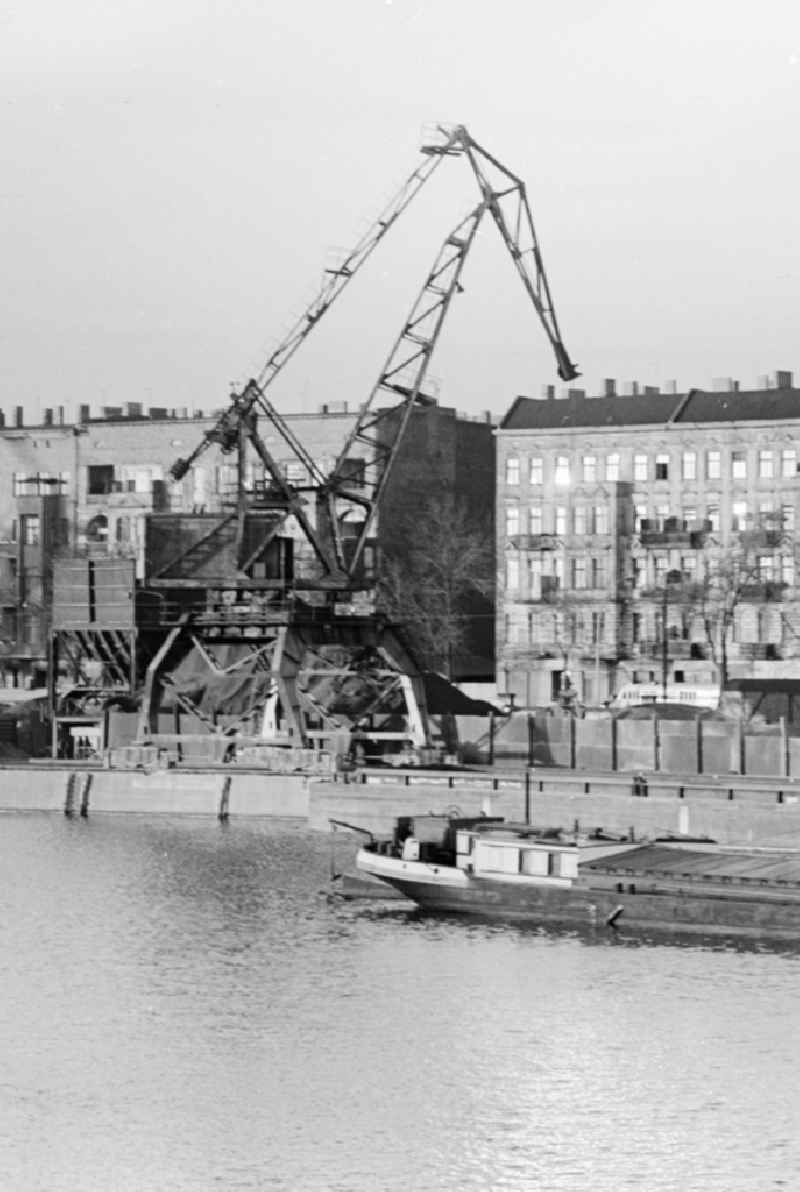 A heavy-duty crane at the riverside in the east port - Port Industry in Berlin. In the background houses at Stralauer Allee. In the foreground a transport barge