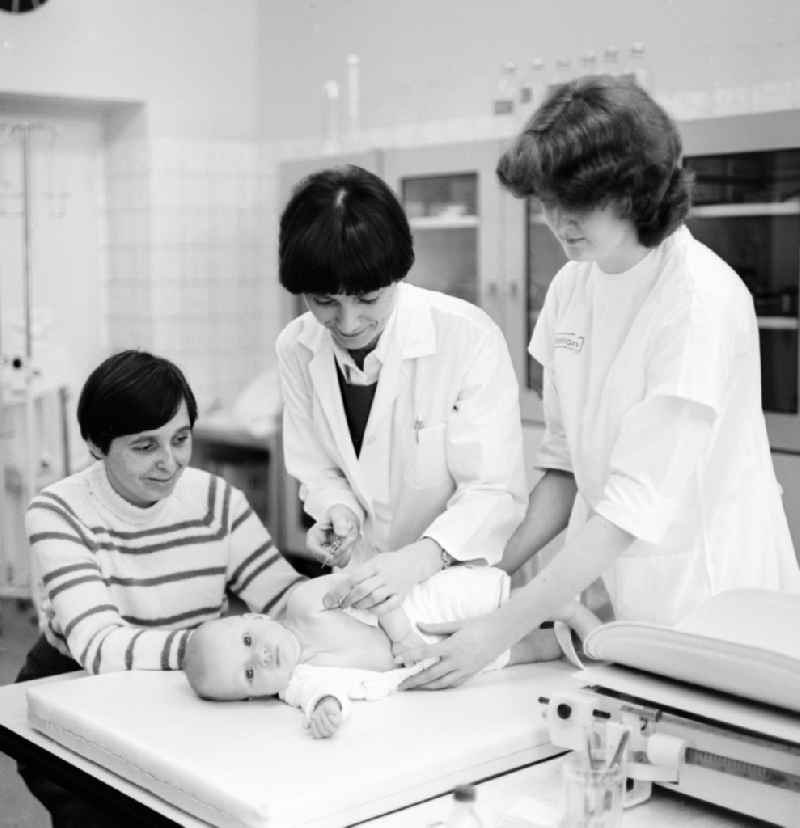 A mother is holding her baby at a check-up in the Children's Clinic in Klinikum Berlin-Buch in Berlin, the former capital of the GDR, the German Democratic Republic. The baby receives a vaccination (vaccination) as a preventive measure