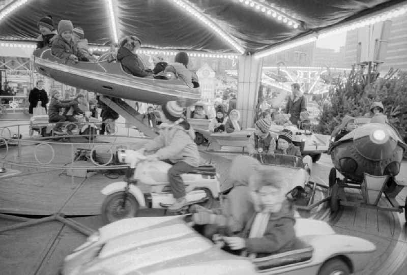 Children sit in a roundabout on the Berlin Christmas fair in Berlin, the former capital of the GDR, German democratic republic. Today there stands at this point the shopping centre 'Alexa'