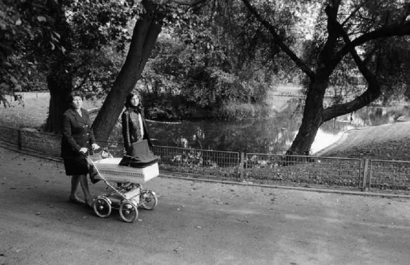 Two women go by a baby carriage in a park walk in Berlin, the former capital of the GDR, German democratic republic