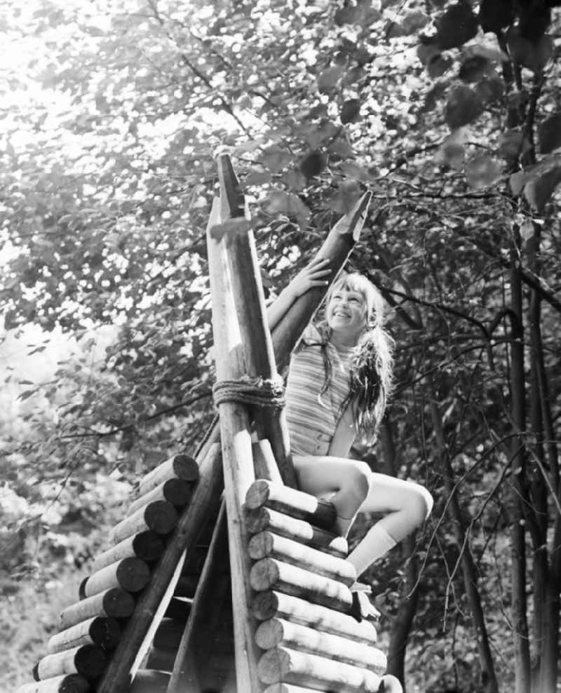 Laughing girl on a wooden tepee on a playground in Berlin, the former capital of the GDR, German democratic republic