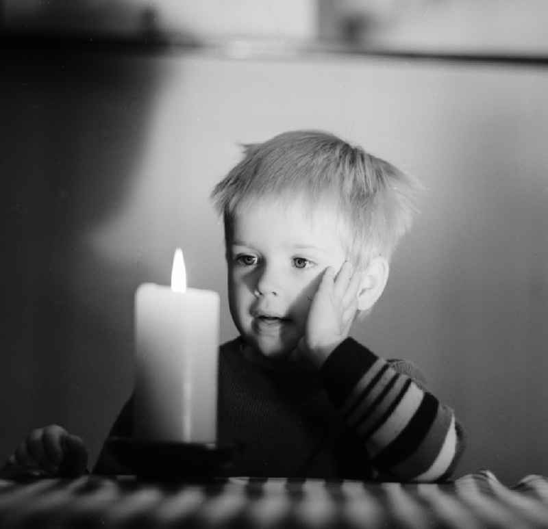 A small child marvels at a burning candle standing on a table in Berlin, the former capital of the GDR, German Democratic Republic