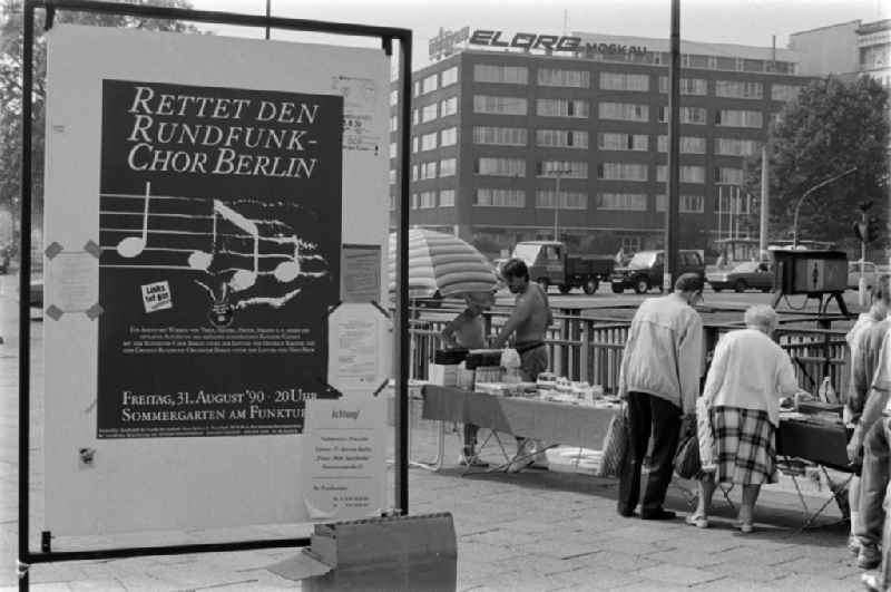 A poster with the words 'Save the Rundfunk-Chor Berlin' stands at the Frankfurter Tor in Berlin - Friedrichshain. In the background, passers-by are standing at a stall