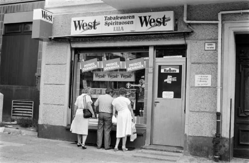 Passers-by are standing in front of a shop for tobacco like 'West', 'Prince Denmark', 'Marlboro' and 'Camel' as well as spirits at the Karl-Marx-Allee in Berlin - Friedrichshain