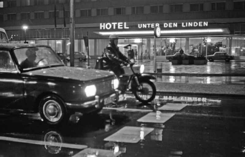 Car - motor vehicle in nighttime and rainy traffic Wartburg 311 and MZ motorcycle in front of the ' Hotel Unter den Linden ' on Friedrichstrasse in the Mitte district of Berlin East Berlin on the territory of the former GDR, German Democratic Republic