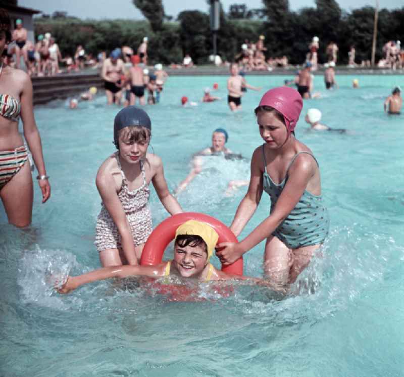 Girls in swimsuits, swimming caps and swimming rings in an outdoor swimming pool on Wolfshagener Strasse in the Pankow district of East Berlin in the territory of the former GDR, German Democratic Republic