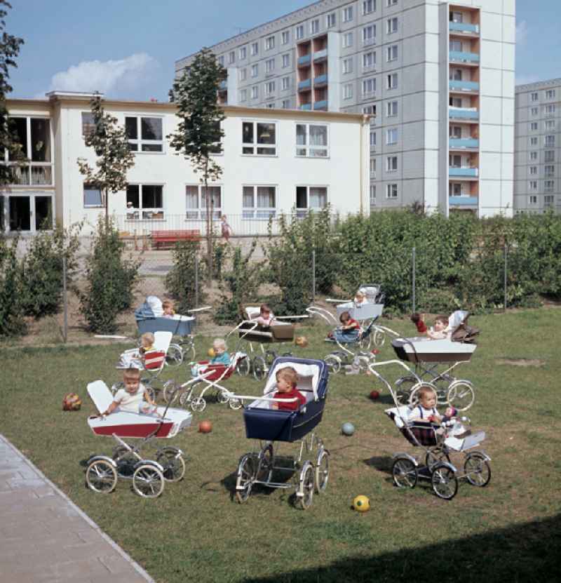 Small children sit in a stroller in the yard of a daycare center in East Berlin in the territory of the former GDR, German Democratic Republic