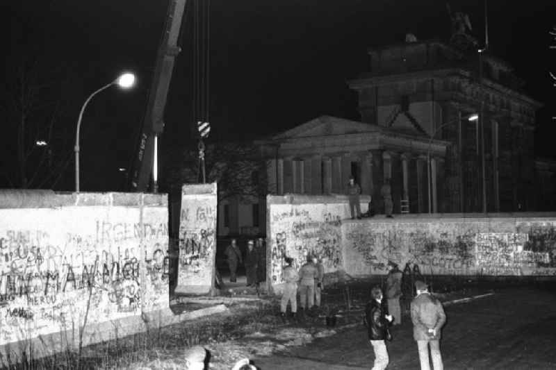 Nachtaufnahme: Maueröffnung / Mauerabbau am Brandenburger Tor. Kran hebt Mauerstück / Mauersegment.