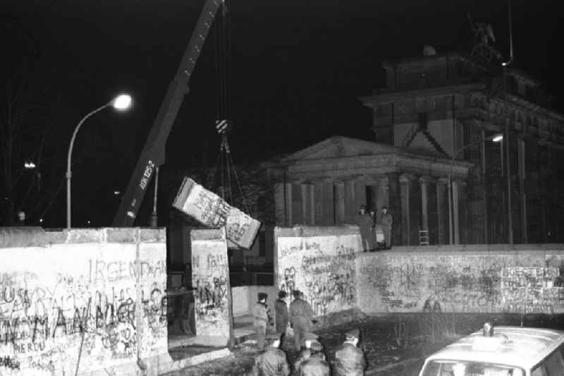 Nachtaufnahme: Maueröffnung / Mauerabbau am Brandenburger Tor. Kran hebt Mauerstück / Mauersegment.