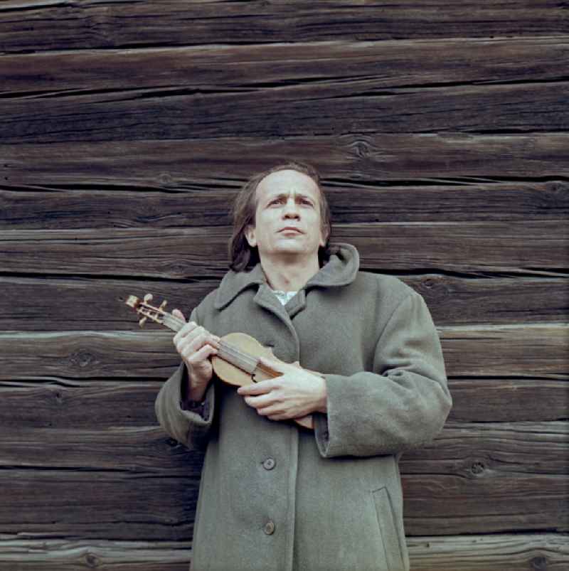 Scene from the film and television production Rublak - The Legend of the Surveyed Land Waste Landscape in Lusatia - the actor Christian Grashof stands with a violin in his arm at the wooden wall of the village church in the Spey district of Boxberg in the GDR