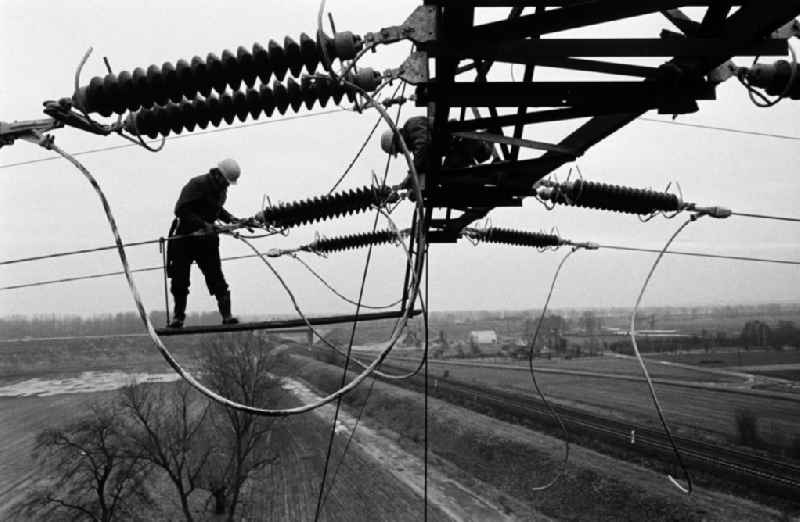 Arbeiter bei der Montage einer Hochspannungsleitung bei Brieselang in luftiger Höhe in Aktion. Die DDR-Energieversorung basiert zu einem großen Teil auf der Verstromung von Braunkohle aus der Lausitz und Sachsen, was unter anderem lange Leitungswege nötig macht.